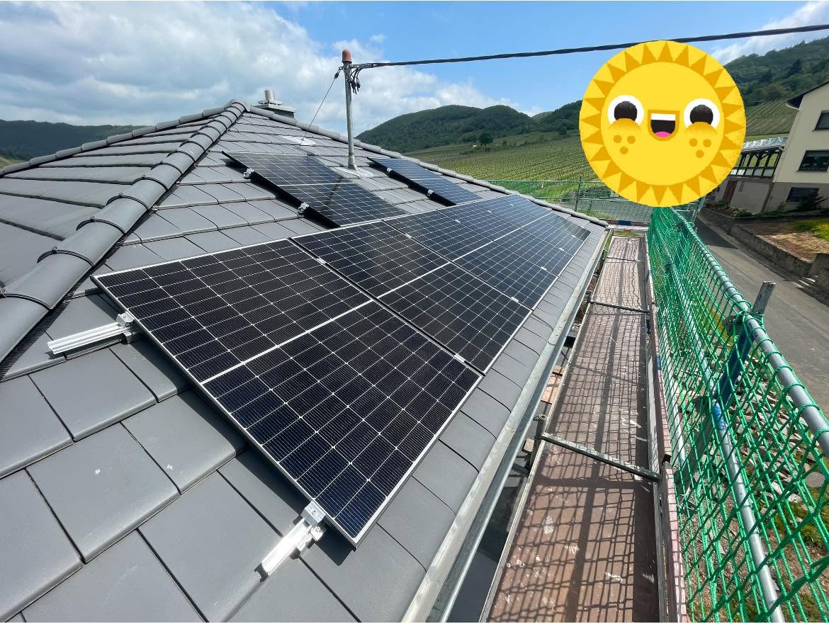 Photovoltaikmodule auf einem grauen Ziegeldach, im Hintergrund Weinberge